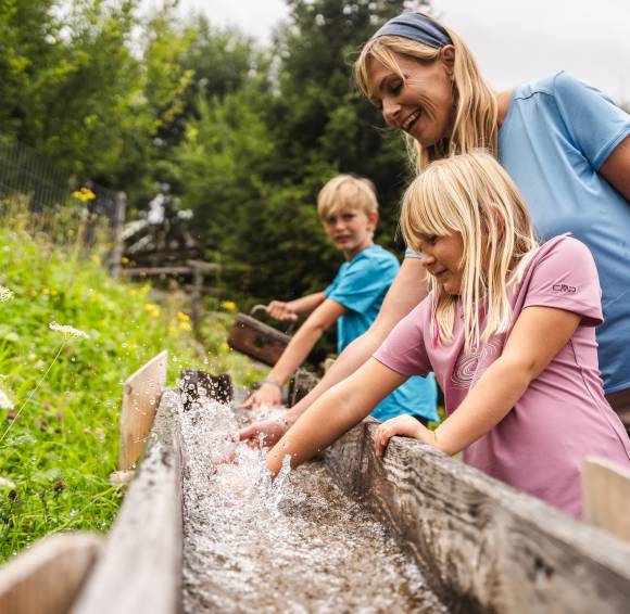 Familie erfrischt ihre Hände in einem Brunnen auf dem Wanderweg
