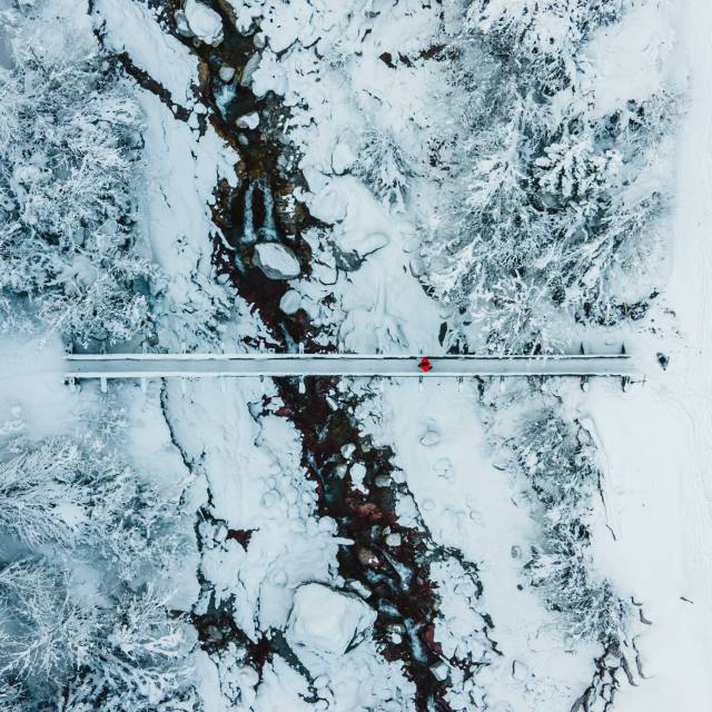 Luftaufnahme einer winterlichen Landschaft mit einer Brücke und Bäumen